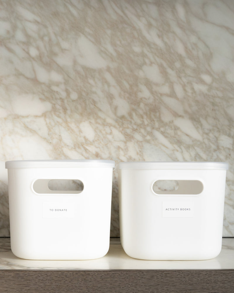 Two white storage bins with handles on a wooden surface against a marble wall.